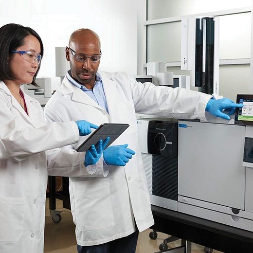 Two scientists in lab discussing content on a tablet and gesturing toward a GC touch screen