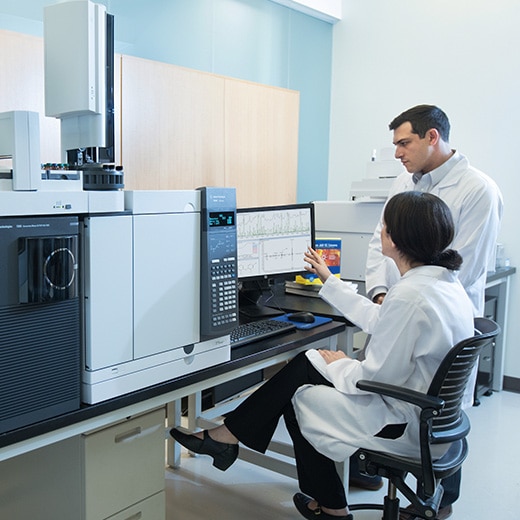 Two scientists holding discussion in lab with multiple GC instruments