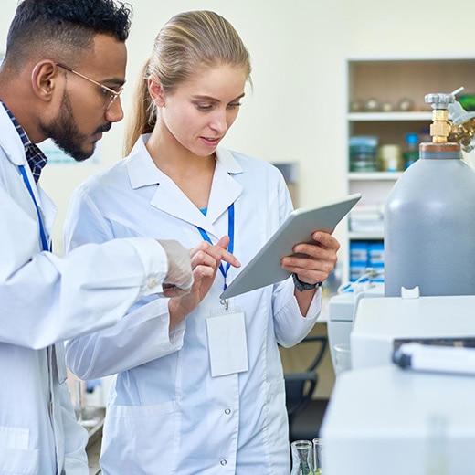 Two lab scientists using tablet beside a GC and helium tanks